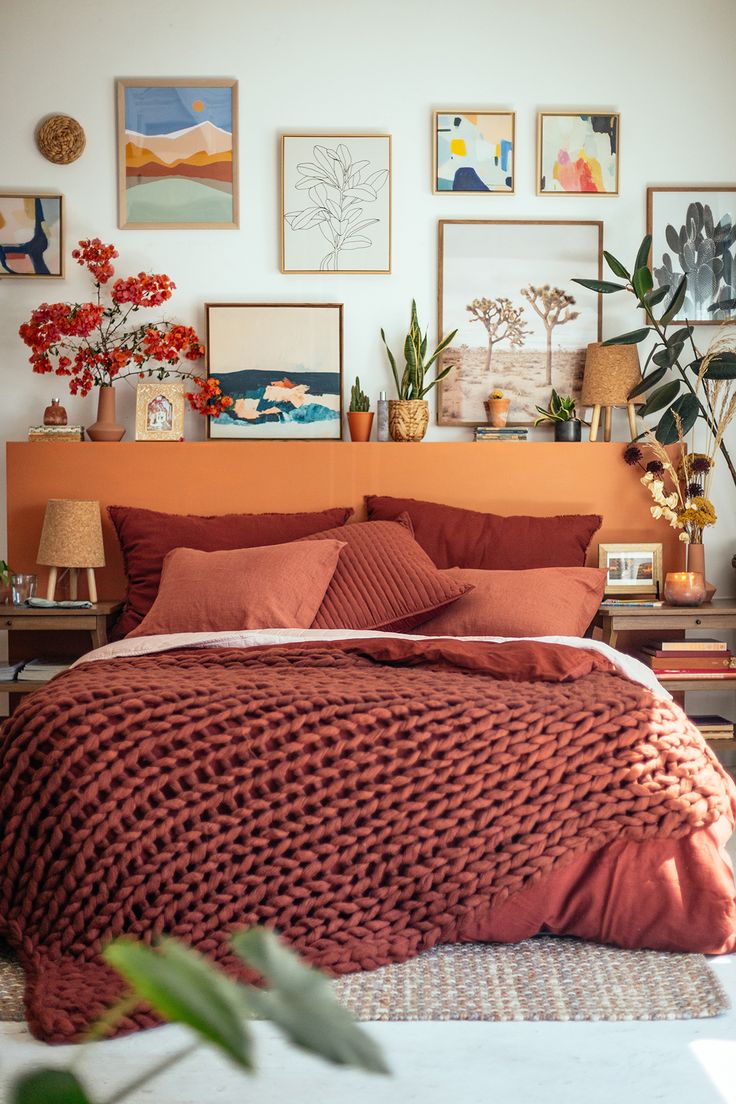 a bed with red sheets and pillows in a room filled with pictures on the wall