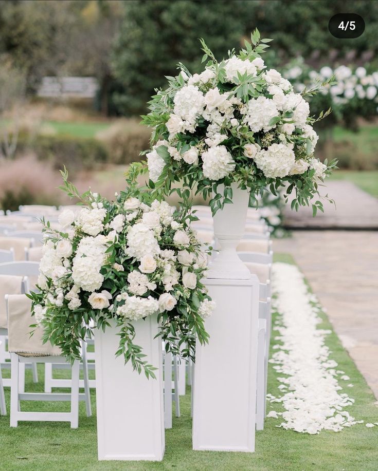 white flowers and greenery decorate tall vases at an outdoor ceremony