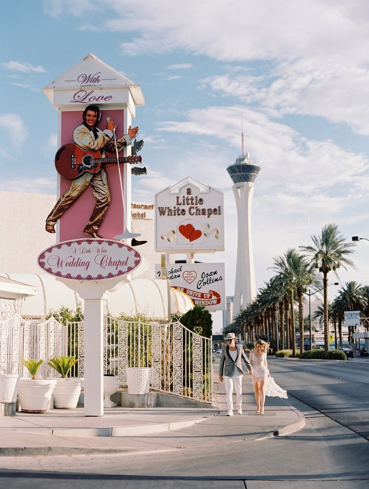 two people walking down the street in front of a sign for elvis's white chapel