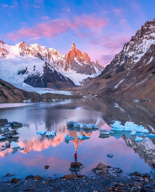 a lake surrounded by mountains with icebergs in the water and rocks around it