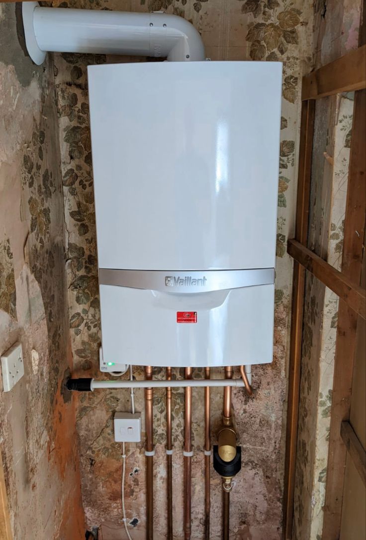 a tankless water heater mounted to the side of a wall next to pipes