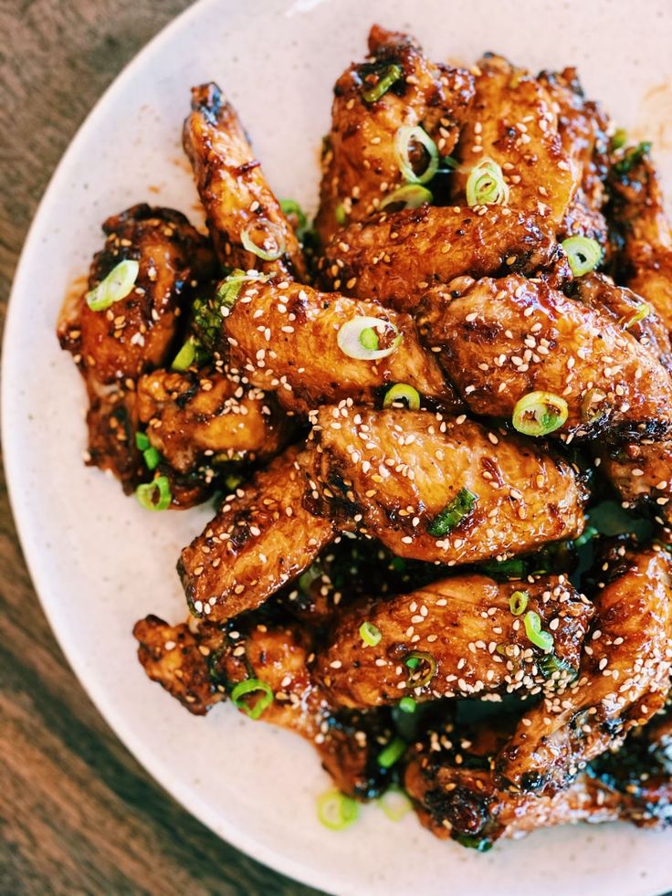 a white plate topped with chicken wings covered in sesame seeds and seasoning sprinkled with green onions