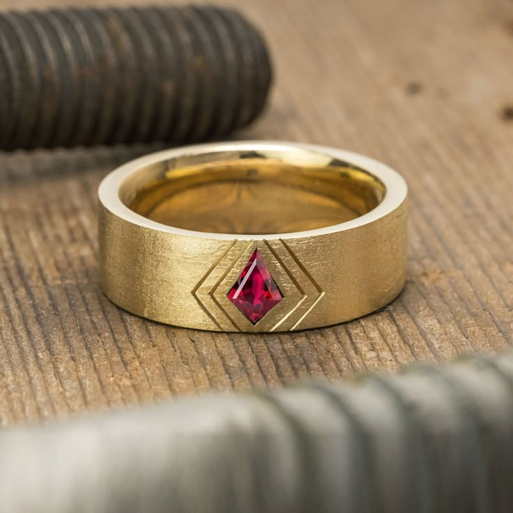 a gold ring with a red diamond in it sitting on the ground next to a pipe