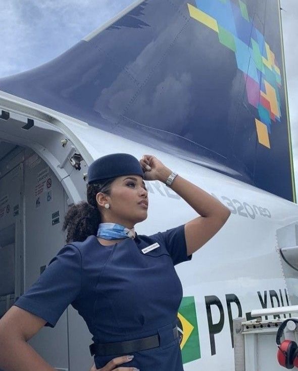 a woman in uniform standing next to the wing of an airplane with her hand on her head