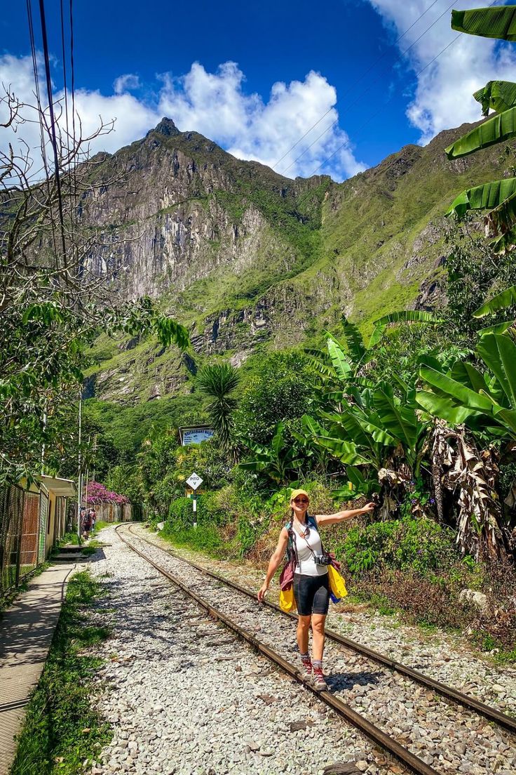 a woman is walking down the railroad tracks in front of some mountains and greenery