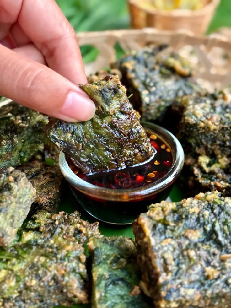 a person dipping something into a small bowl filled with sauce on top of green leaves