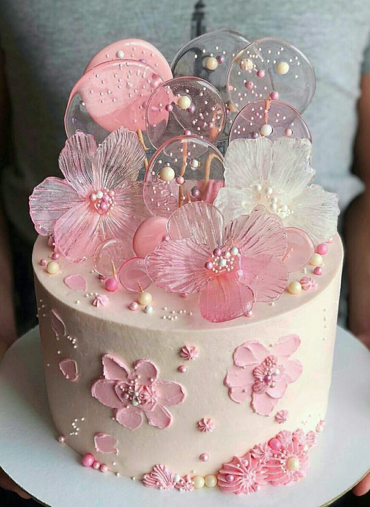 a pink and white cake with lots of flowers on the top is sitting on a plate