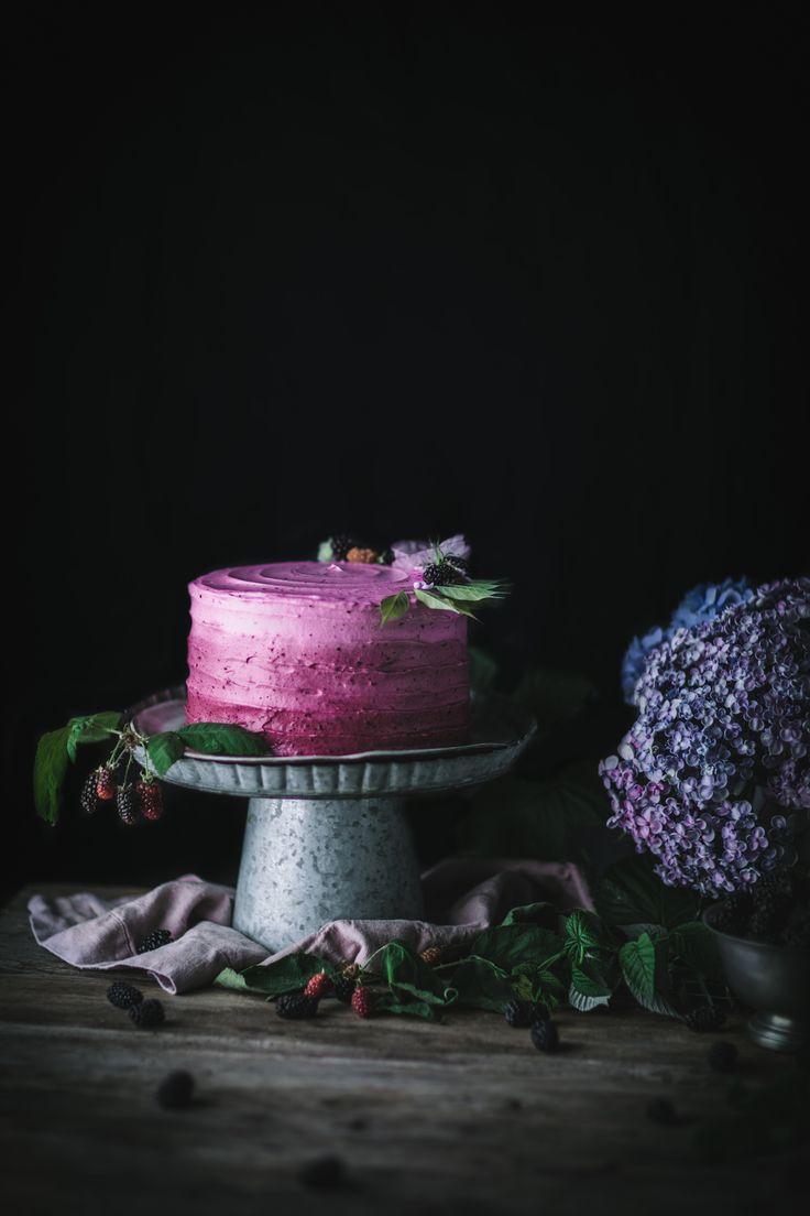 a pink cake sitting on top of a wooden table next to purple and green flowers