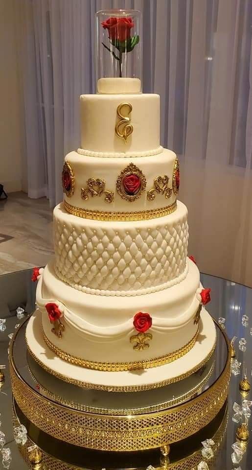 a three tiered white wedding cake with red roses on the top and gold trimmings