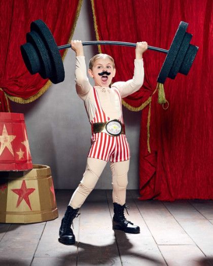 a young boy is performing with a barbell in front of red curtained curtains