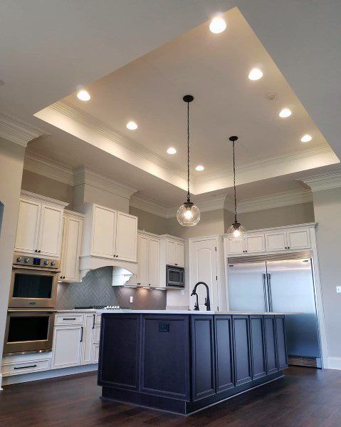 a large kitchen with white cabinets and dark wood flooring, lights above the island