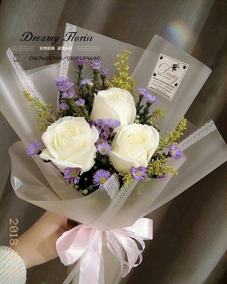 a bouquet of white roses and lavenders wrapped in clear cellophane with ribbon