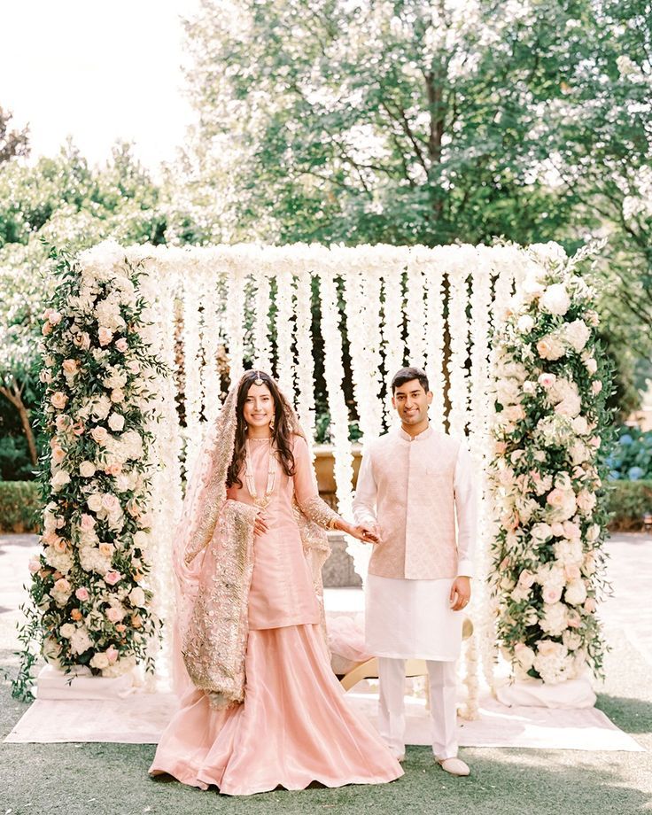 a man and woman standing in front of a floral arch