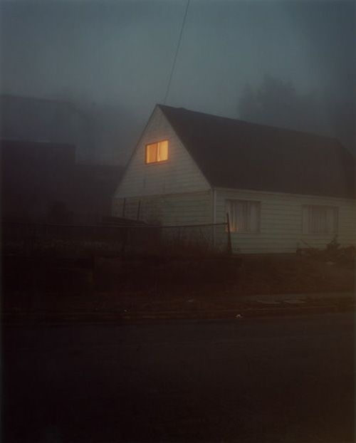 a white house sitting on the side of a road at night with lights coming from windows