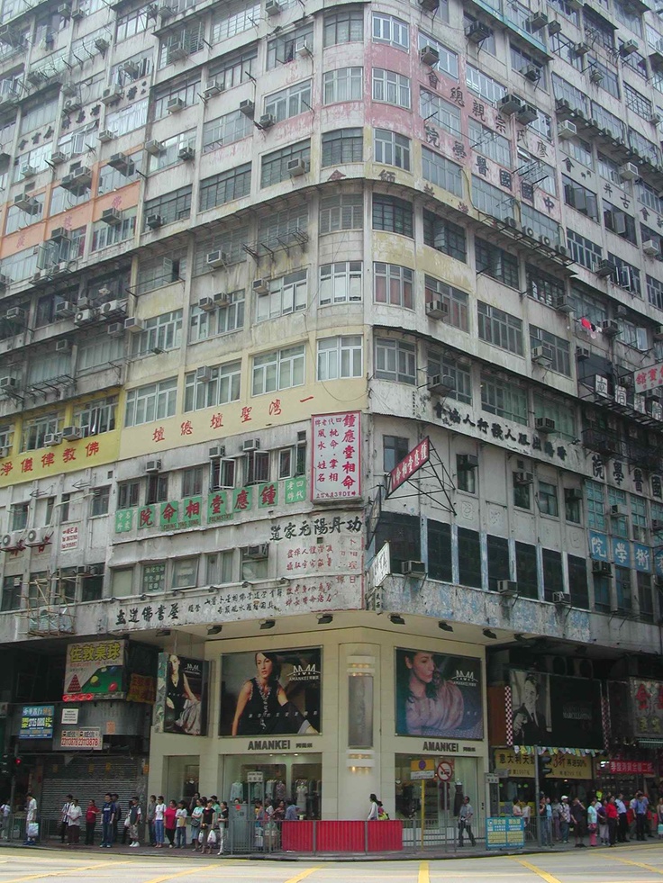 a tall building with lots of windows and people standing in front of it on the sidewalk