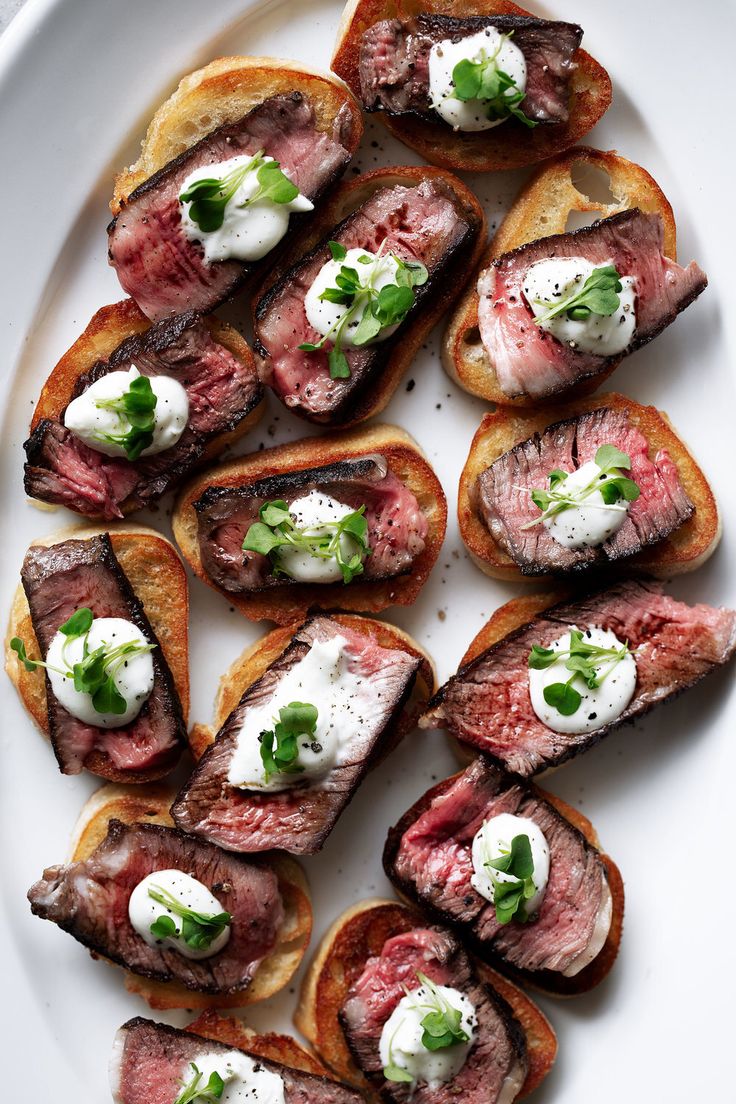 a white plate topped with slices of toasted bread covered in meat and sour cream