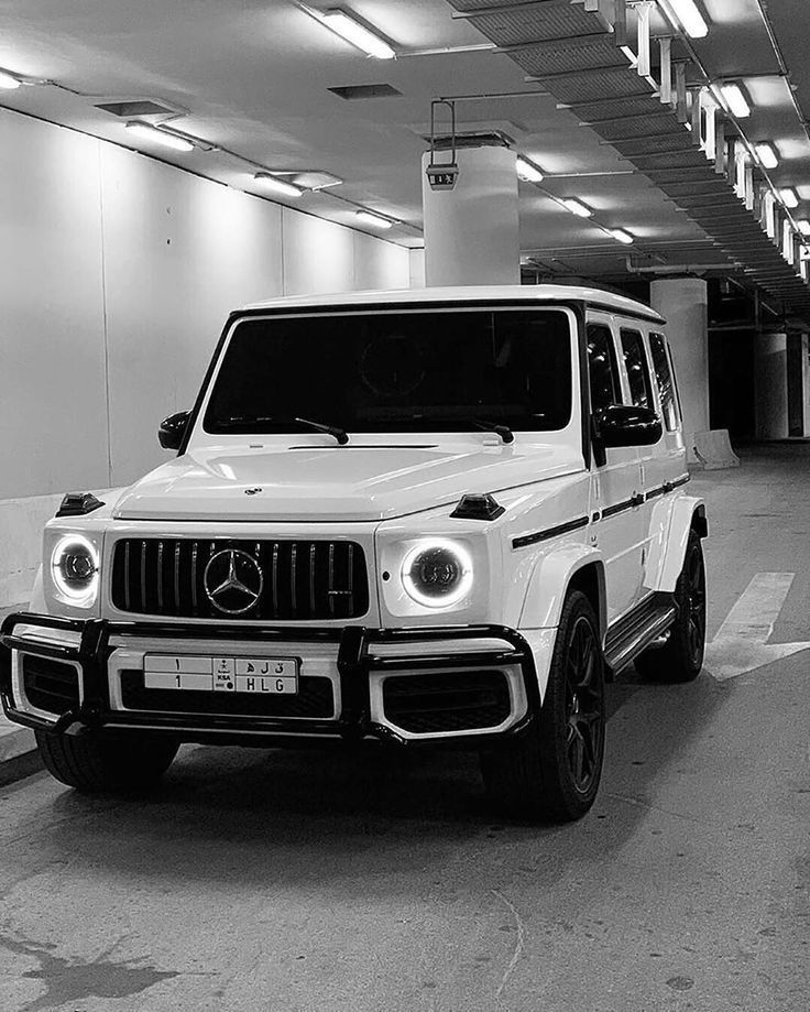 black and white photograph of a mercedes g - class parked in a parking garage with lights on