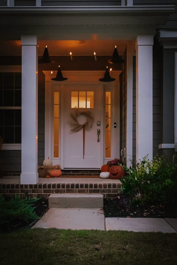 the front door of a house with pumpkins on the steps and lights in the windows