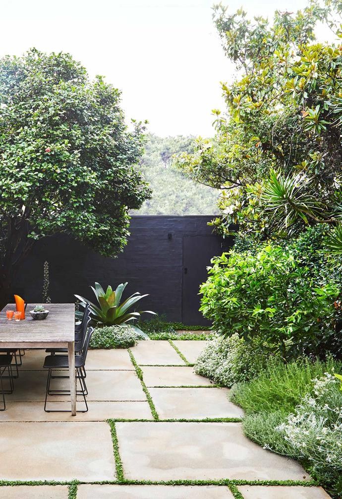 an outdoor dining table and chairs in a small garden area with trees, shrubs, and grass