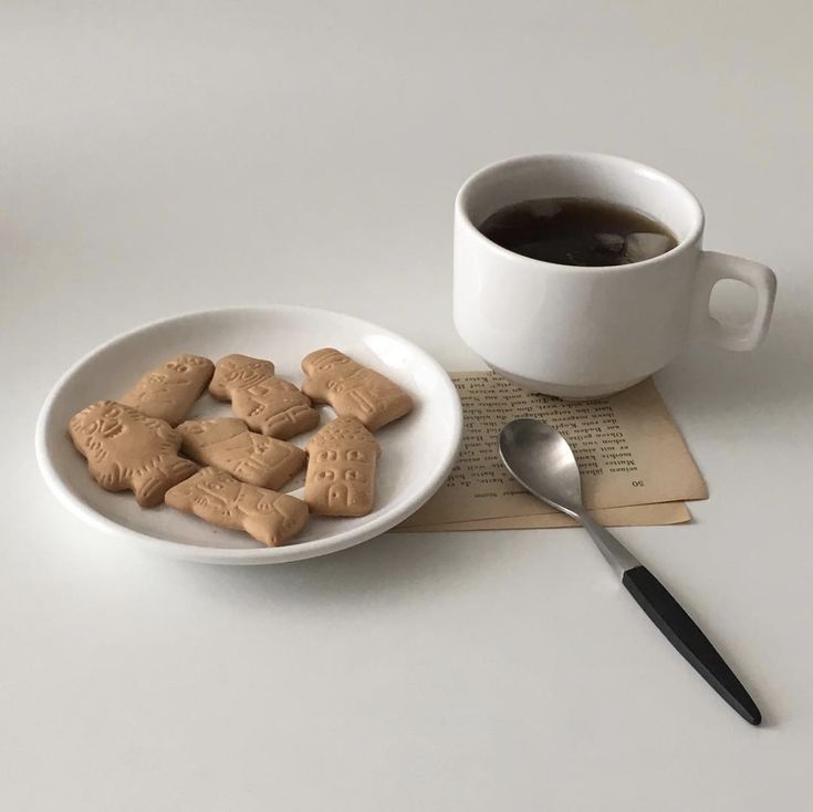 a cup of coffee and some cookies on a plate next to a book with a spoon