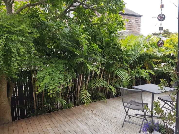 a table and chairs on a wooden deck surrounded by trees, bushes and other greenery