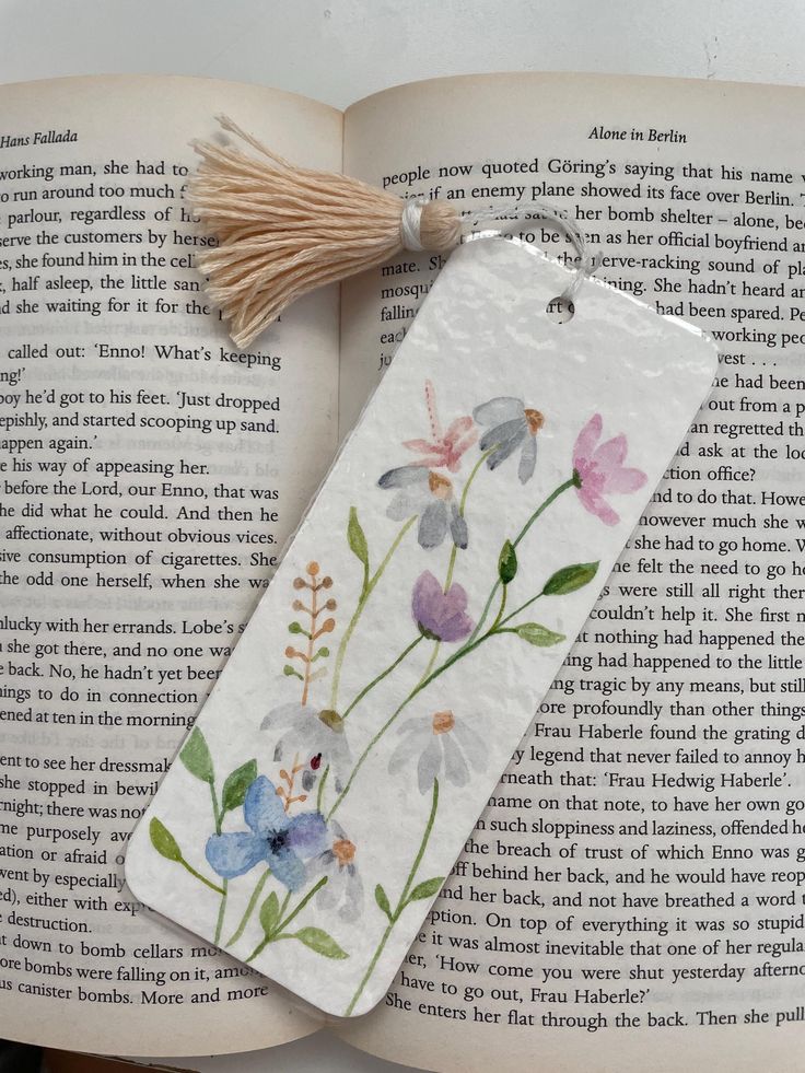 a bookmark with flowers painted on it and tasseled to the back of an open book