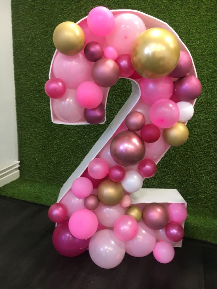 the number two made out of balloons in front of a green wall with artificial grass