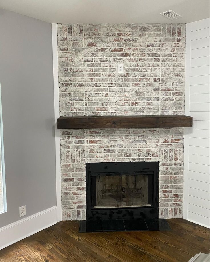 an empty room with a brick fireplace and wood floors in the corner, painted white