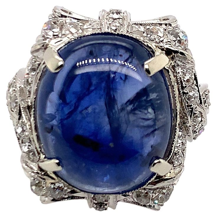 The bold design set with a cabochon sapphire weighing approximately 14.00 carats, framed by elaborate ribbon bows and sash motifs set with round diamonds, in 18k white gold, size 5 1/2 Weight: 9.2 grams Sapphire measuring 15.19 x 12.90 x 5.56 mm, of a medium light tone of slightly violetish blue colour, noticeably included, good cut Diamonds estimated weight 0.75 carat, G-I colour, VS-I1 clarity Good condition Luxury Sapphire-colored Diamond Ring With Diamond Cut, Luxury Oval Cabochon Sapphire Ring, Luxury Blue Cabochon Sapphire Ring, Luxury Sapphire Cabochon Ring, Luxury Sapphire Ring, Oval Cabochon Cut, Domed Ring, Sapphire Diamond, Ribbon Bows, White Gold Rings