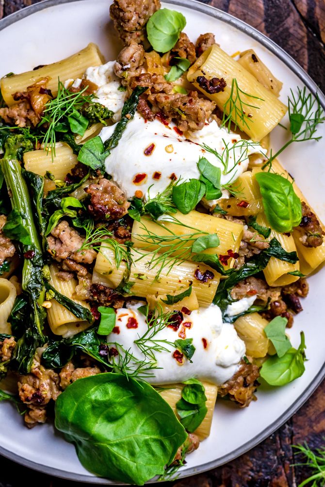 a white plate topped with pasta and meat covered in cheese, spinach leaves and sour cream