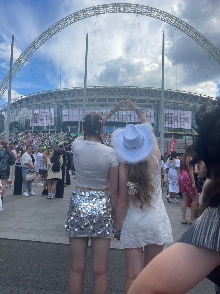 two women in sequin skirts and hats are looking at the stadium from behind them