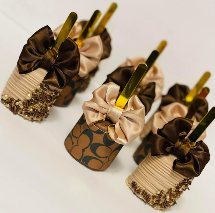 there are four decorated cupcakes with gold and brown bows