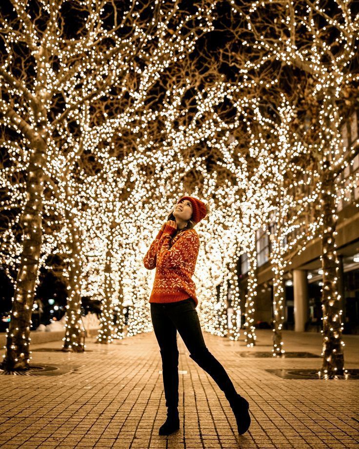 a woman standing in front of trees covered with lights