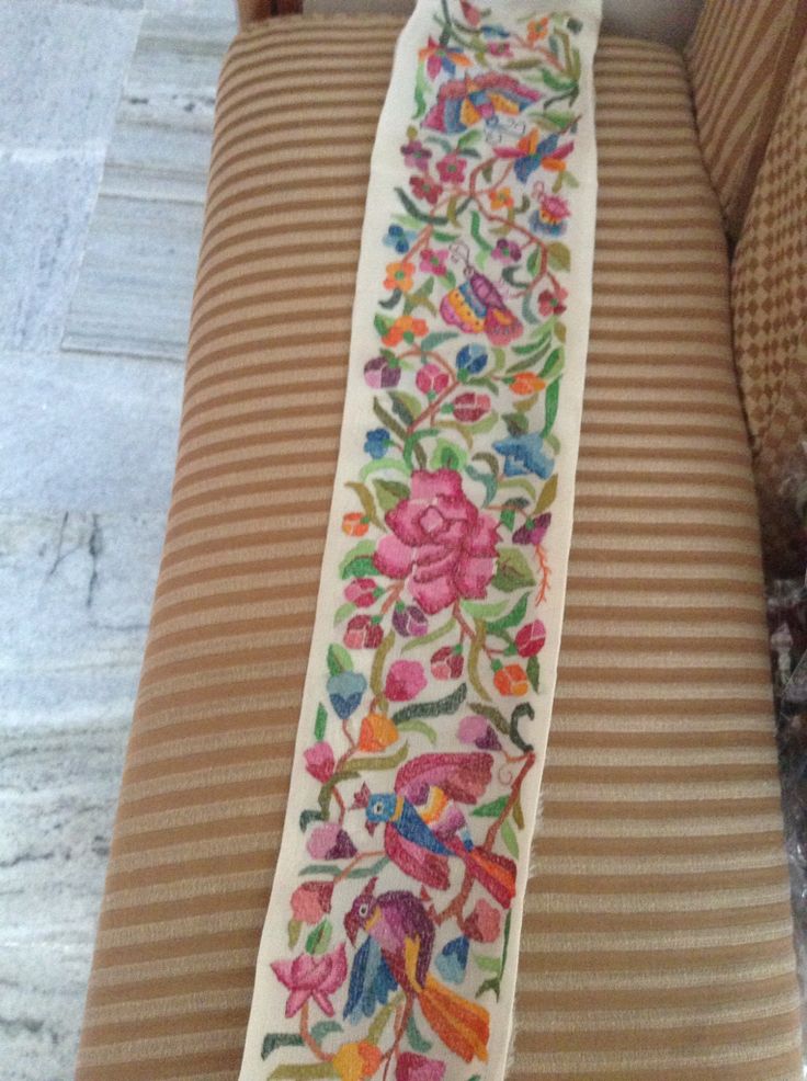 an embroidered tie with flowers on it sitting on top of a chair next to a pillow