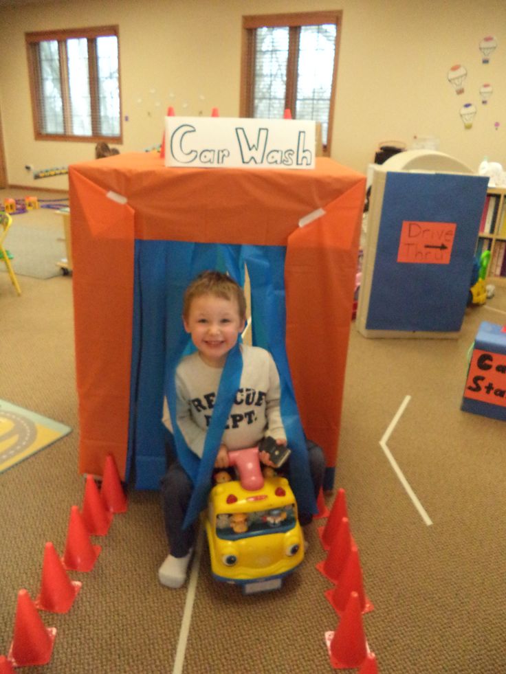 a young boy sitting in a toy car with an orange cover over his head and smiling at the camera