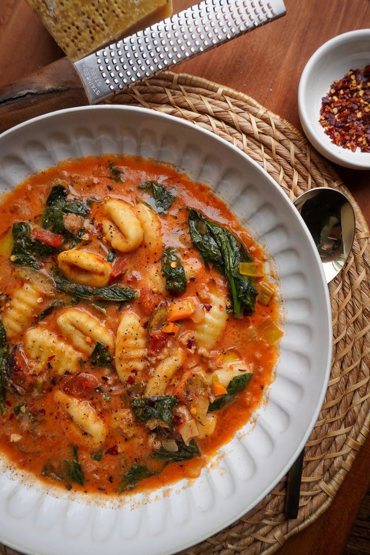 a white plate topped with pasta and spinach next to a bowl of bread on top of a wooden table