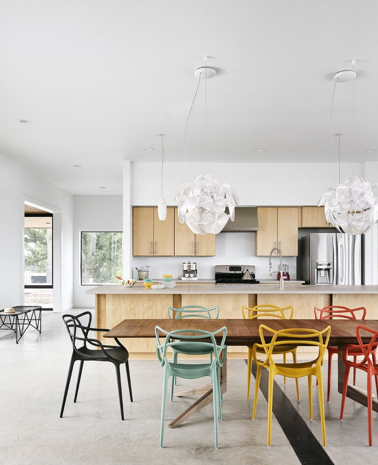 a dining room table surrounded by chairs in front of an open kitchen with lots of windows