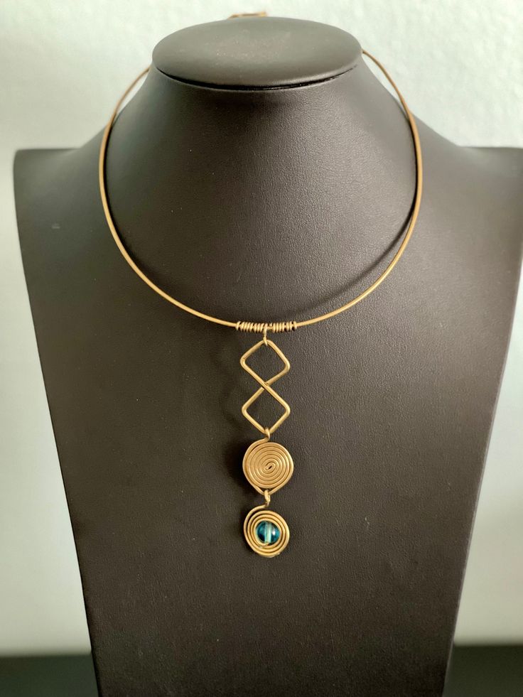 Unique bold brass choker. This piece is composed of a simple, elegant wire choker with a long dangle with a diamond and spiral shaped motif and a single blue glass cabochon.  The piece is a combination of modern and ancient boho influences. It's an eclectic statement piece. As with all vintage items there are signs of age and wear. The wire can bend and can be adjusted to fit the wearer. Please inspect photos carefully. Wire Wrapped Metal Dangle Necklaces, Adjustable Wire Wrapped Metal Necklaces, Handmade Metal Dangle Choker, Adjustable Brass Choker With Chain, Bohemian Adjustable Wire Necklaces, Adjustable Brass Chain Choker, Bohemian Adjustable Wire Necklace, Adjustable Bohemian Wire Necklace, Adjustable Brass Wire Wrapped Necklaces