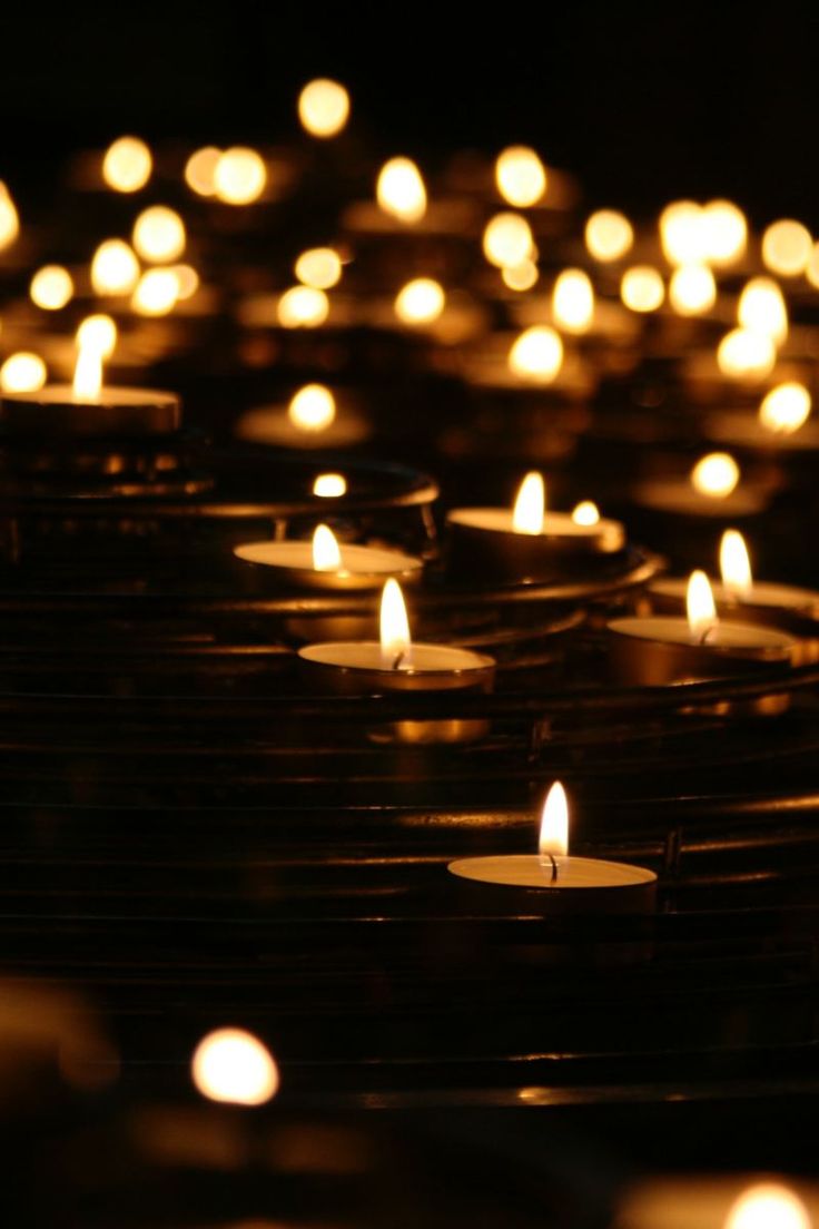 rows of lit candles are shown in the dark