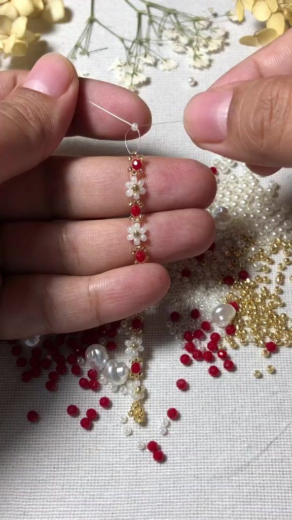 two hands are working on beading with red and white beads in the middle of them