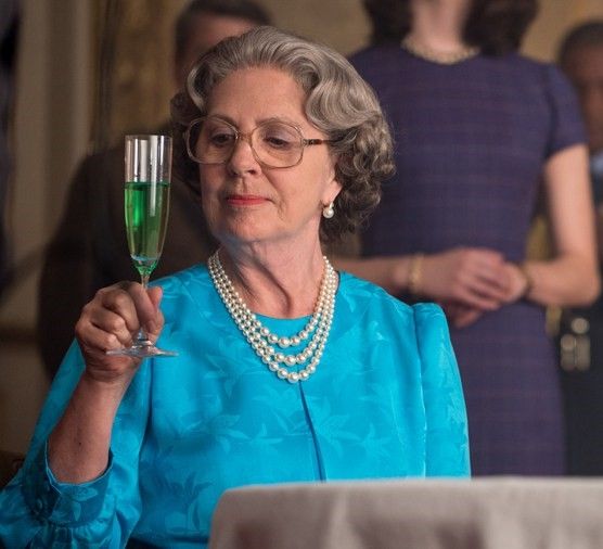 an older woman holding a wine glass in front of other people