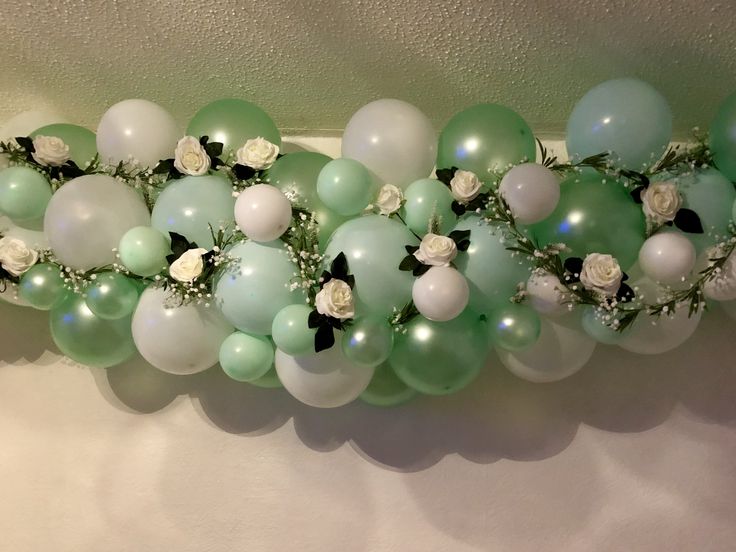 some balloons are hanging on the wall with flowers and pearls around them, as well as white roses