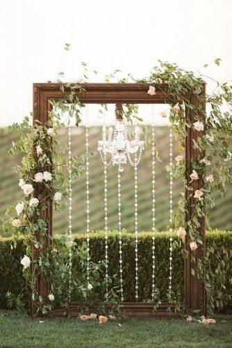 a wooden frame with white flowers and pearls hanging from it is surrounded by greenery