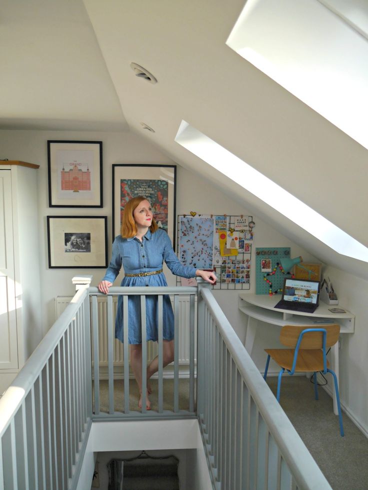 a woman standing on top of a stair case in a room filled with pictures and paintings