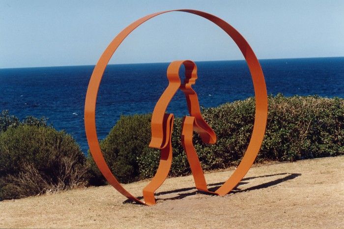 an orange sculpture is in front of the ocean