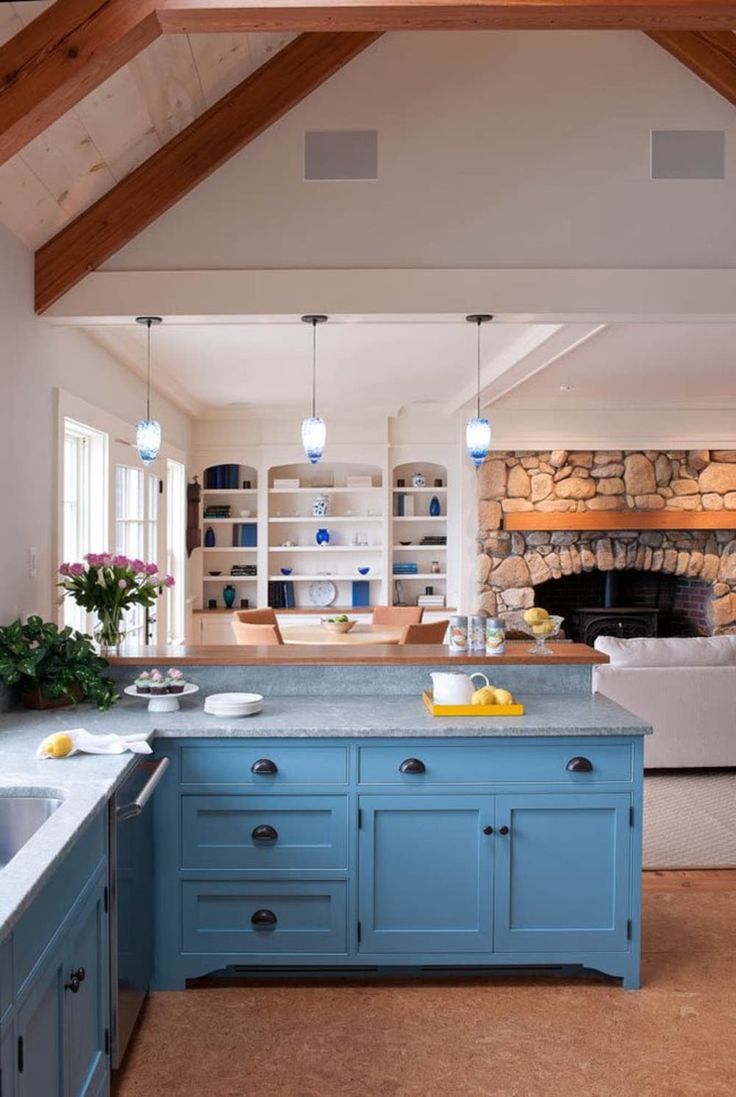 a kitchen with blue cabinets and an island in front of a stone fire place that is built into the wall