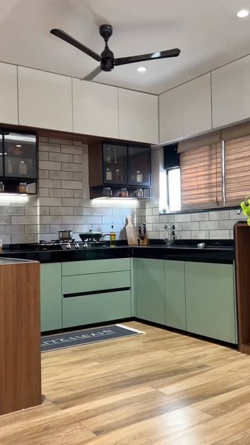 a modern kitchen with green cabinets and wood flooring is seen in this image, the ceiling fan has been turned on