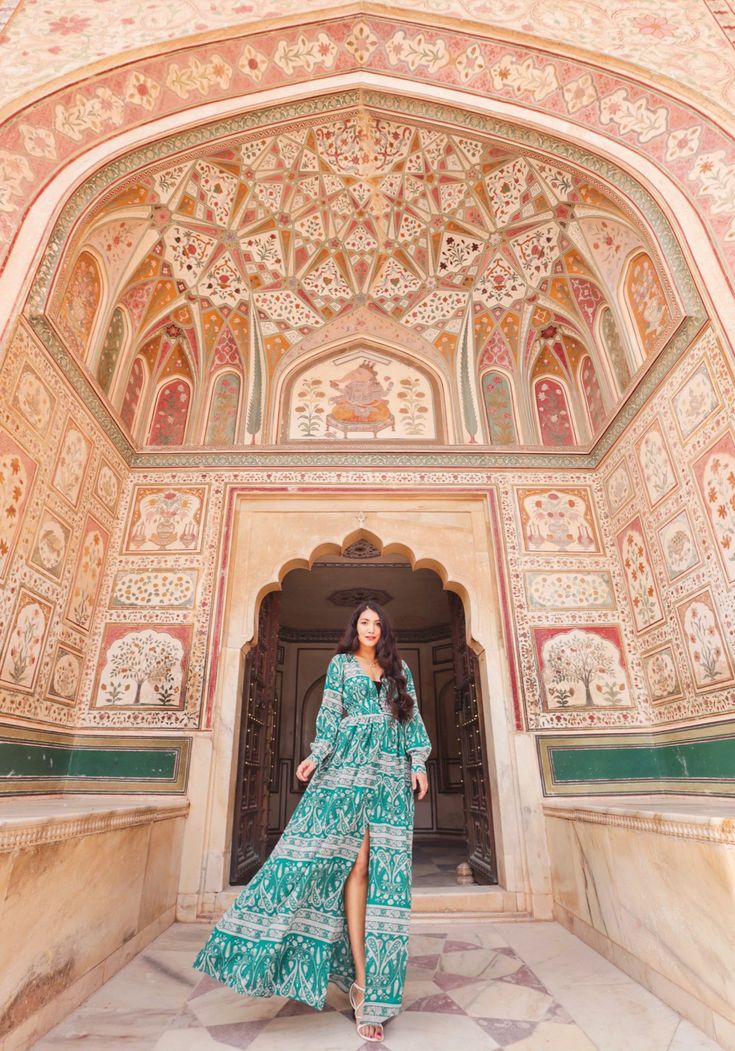 a woman standing in front of an ornate doorway wearing a long green dress and sandals