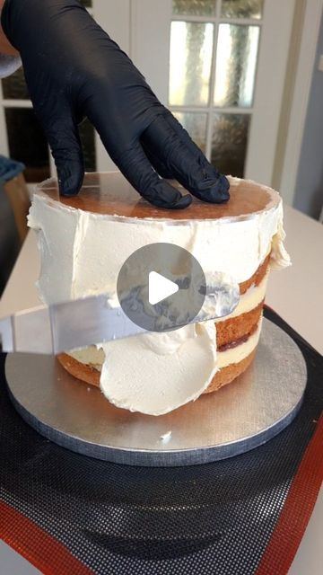 a person in black gloves cutting a cake with white frosting and icing on it