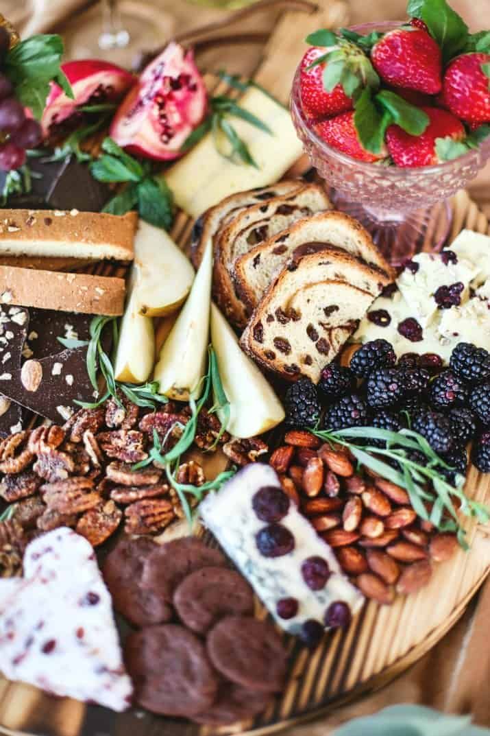 an assortment of cheeses, crackers, nuts and fruit on a wooden platter